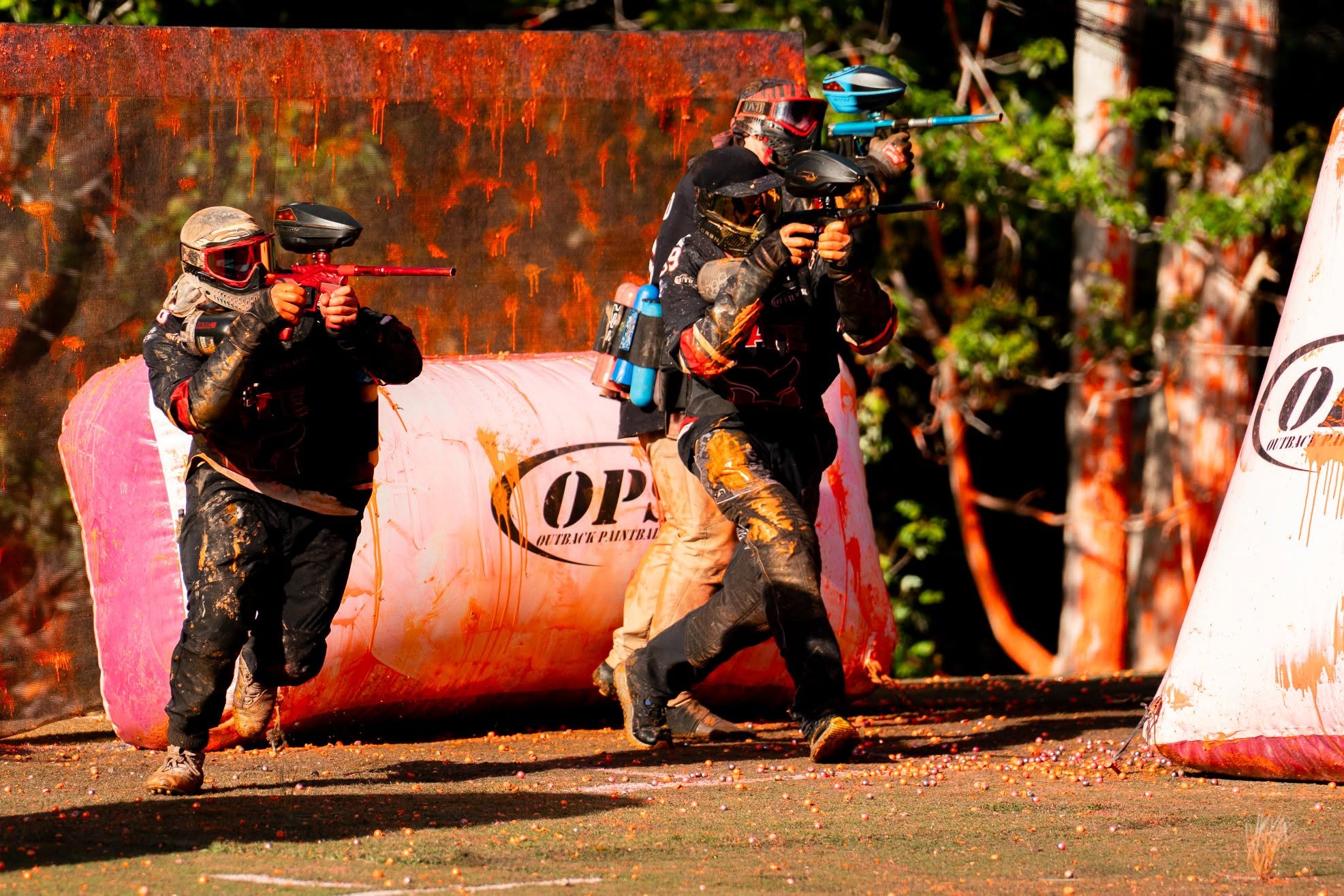 Three players advancing past OPS bunkers under orange paint fire