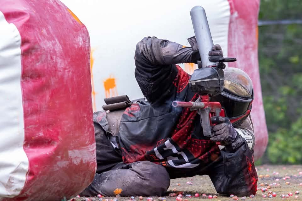 Player low behind a red and white bunker on the speedball field